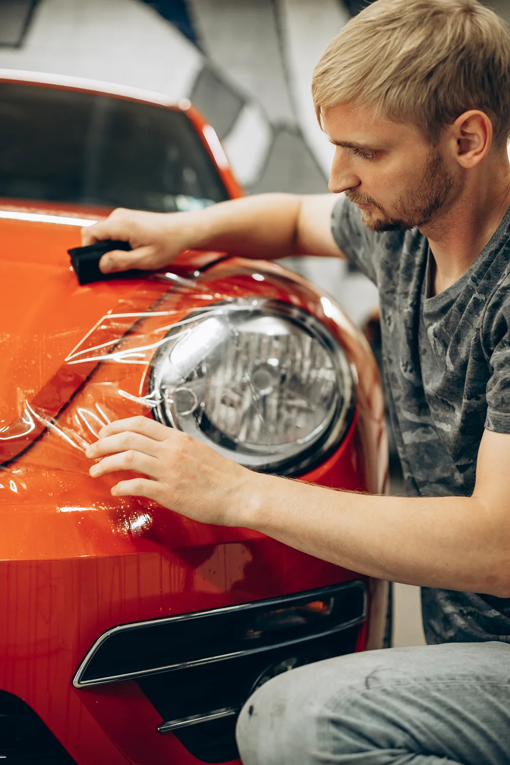 Technician applying paint protection film to an orange sports car